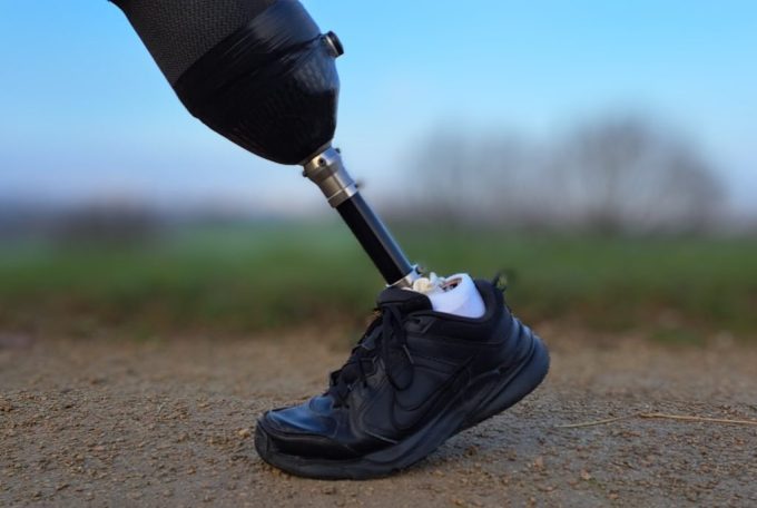 A black sports shoe alongside a prosthetic limb on a path outdoors.