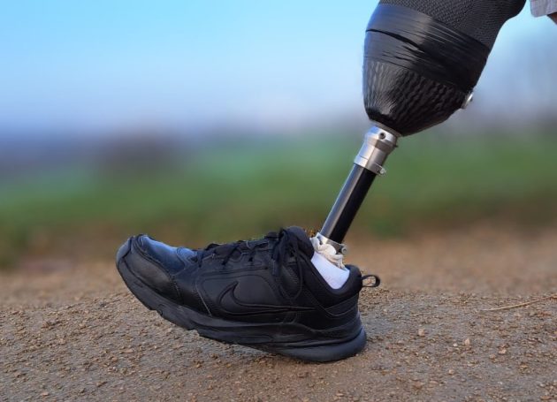 A close-up of a black sneaker worn with a prosthetic leg on a dirt path.